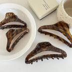 Four tortoiseshell claw hair clips laid out on a white surface, with a decorative bowl and box.