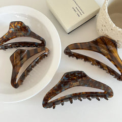 Four tortoiseshell claw hair clips laid out on a white surface, with a decorative bowl and box.