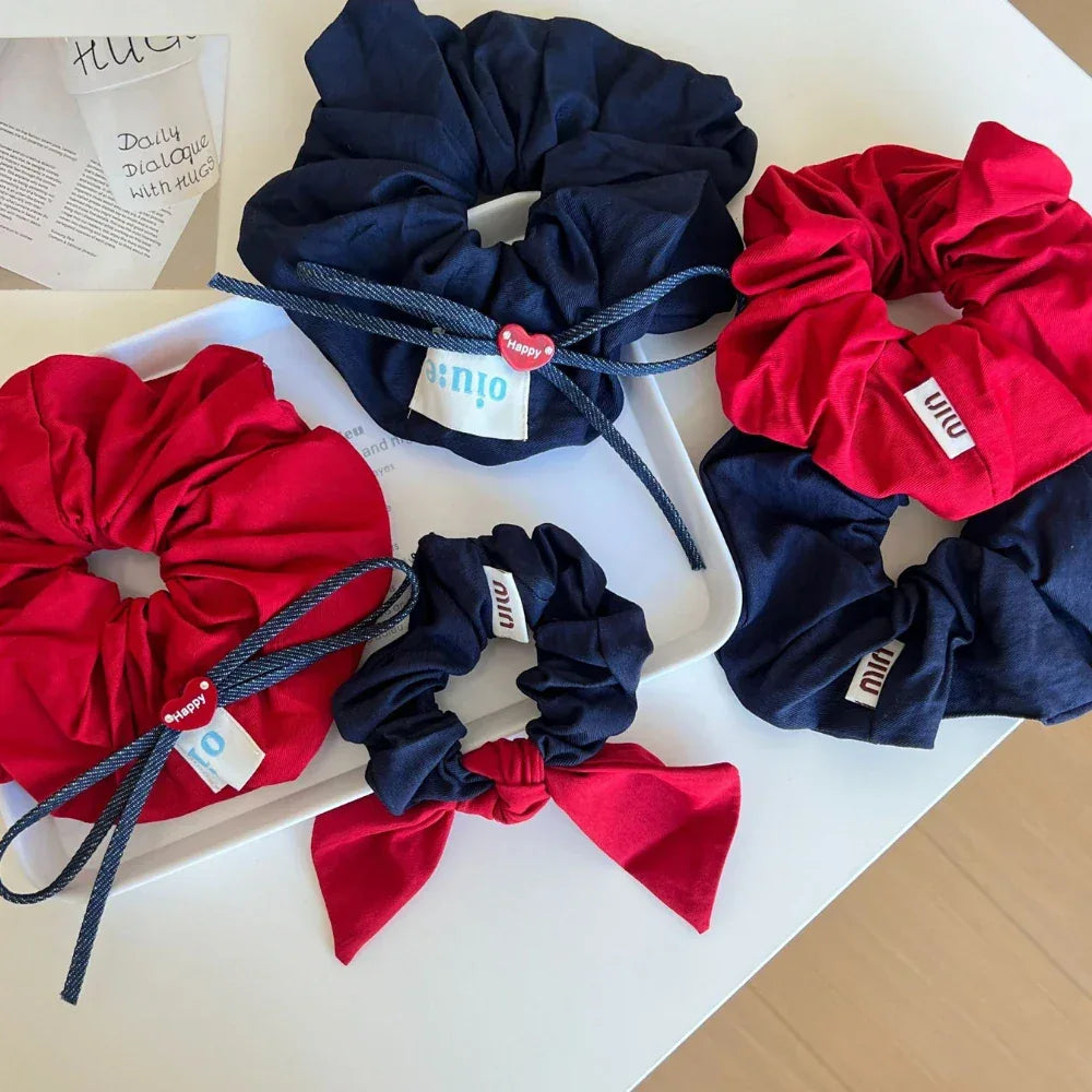 Assortment of red and navy scrunchies, some with bows and heart charms, arranged on a white surface