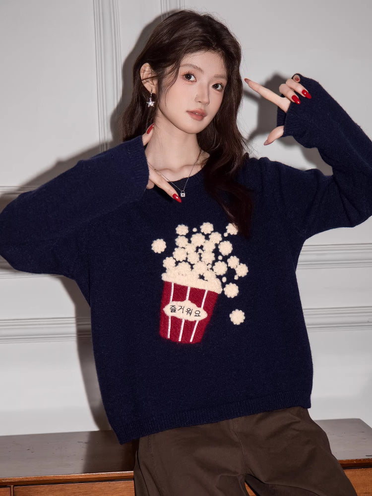Woman wearing a navy blue knit sweater with a popcorn graphic and Korean text, striking a pose.