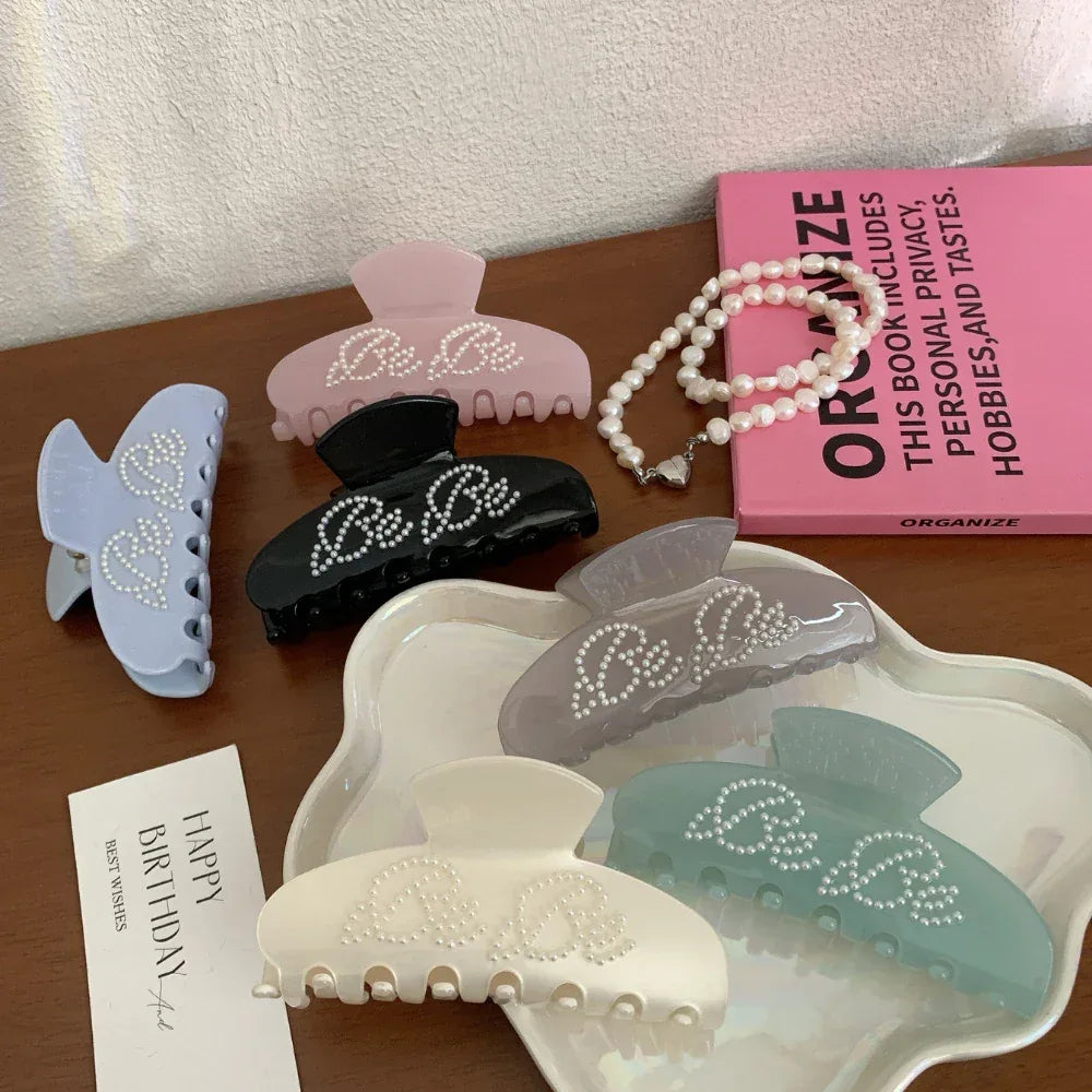 A flat lay of various colored claw clips with pearl-like stud embellishments, a pink book, and a pearl necklace.