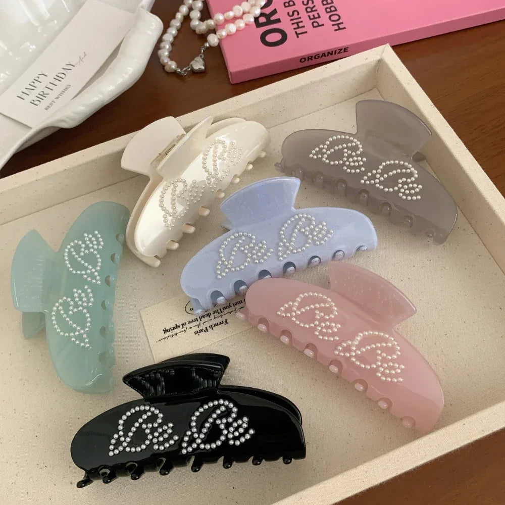 A tray filled with different colored claw clips, all adorned with "Be Be" lettering and pearl-like studs.