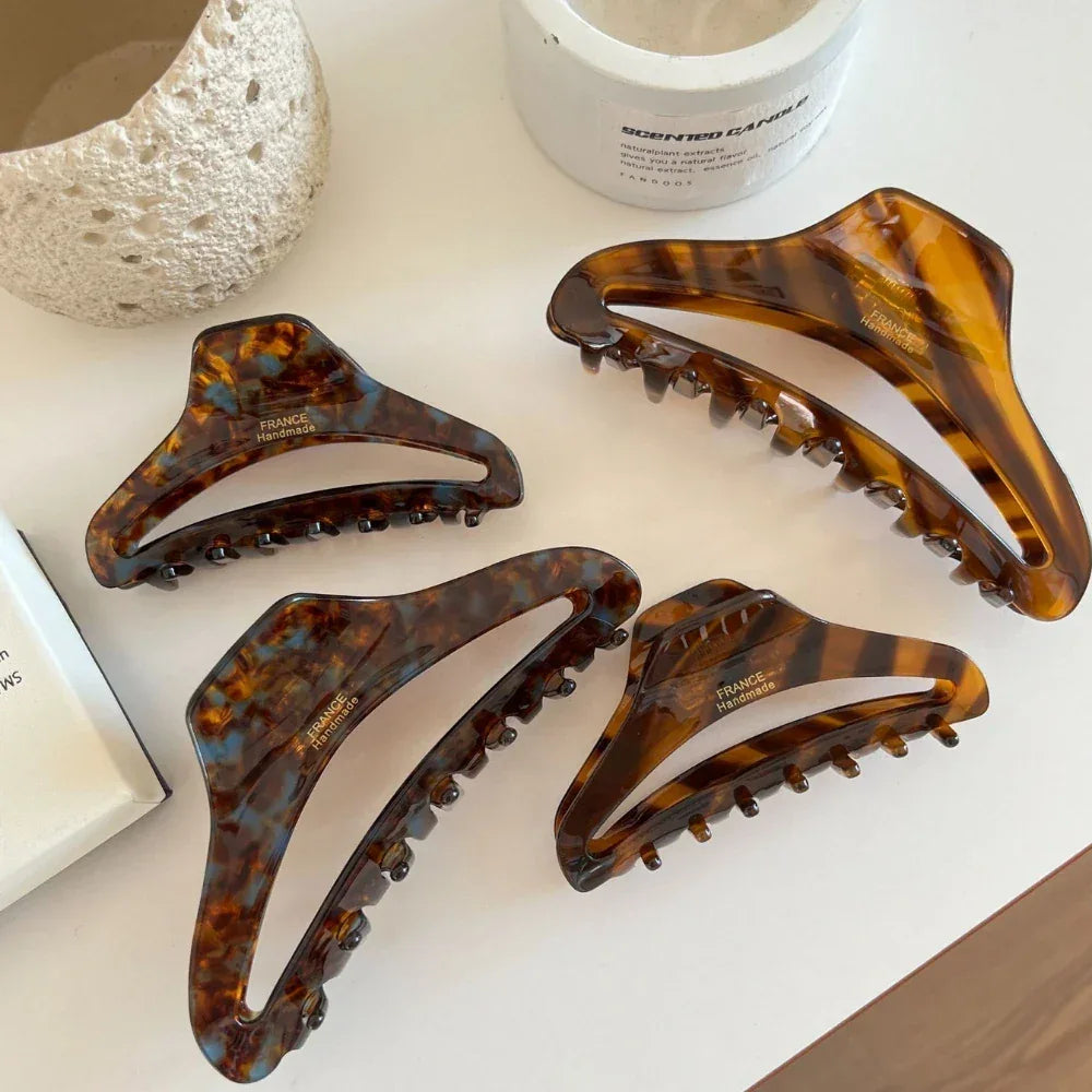 A collection of four tortoiseshell claw hair clips displayed on a white table.