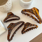 A collection of four tortoiseshell claw hair clips displayed on a white table.