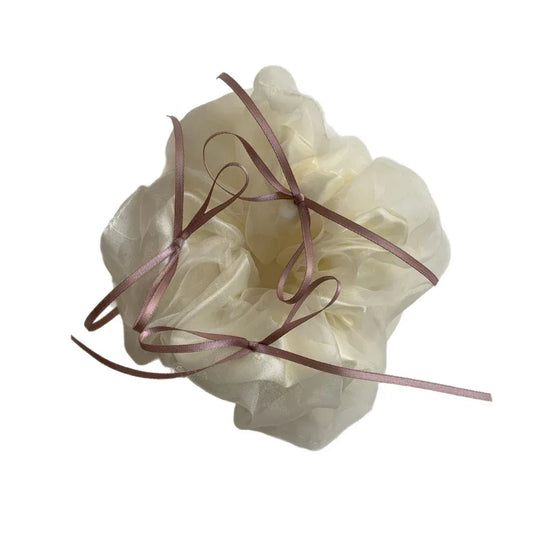 Close-up of an oversized ivory scrunchie with delicate pink ribbon ties.