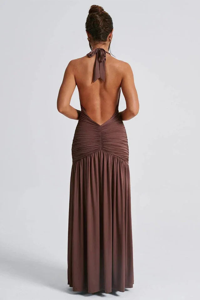 back view of a woman wearing a brown halter maxi dress with an open back and ruched detailing, showing the length of the dress