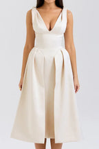 Woman wearing an ivory midi dress with a deep V-neck and pleated skirt.