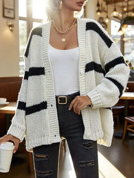 Woman wearing a white and black striped knit cardigan with a white tank top and dark wash jeans.