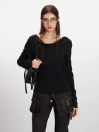 Woman holding a black handbag while wearing a black asymmetrical knit sweater.