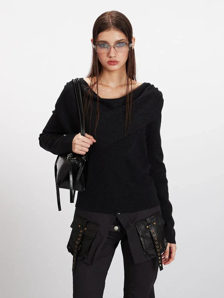Woman holding a black handbag while wearing a black asymmetrical knit sweater.