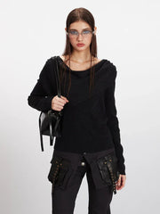 Woman holding a black handbag while wearing a black asymmetrical knit sweater.
