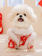 Front view of a white poodle dog wearing a red and white festive coat with embroidered floral patterns, with its mouth open and tongue out.