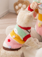A person holds a cream-colored cat wearing a colorful striped sweater, showing the embroidered and appliqued details.