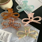 overhead view of bow hair claw clips in blue, amber, pink, and brown on a black surface with text