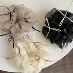 A top-down arrangement of three voluminous scrunchies in ivory, taupe, and black, highlighted by their ribbon embellishments.