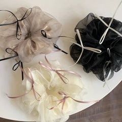 A top-down arrangement of three voluminous scrunchies in ivory, taupe, and black, highlighted by their ribbon embellishments.