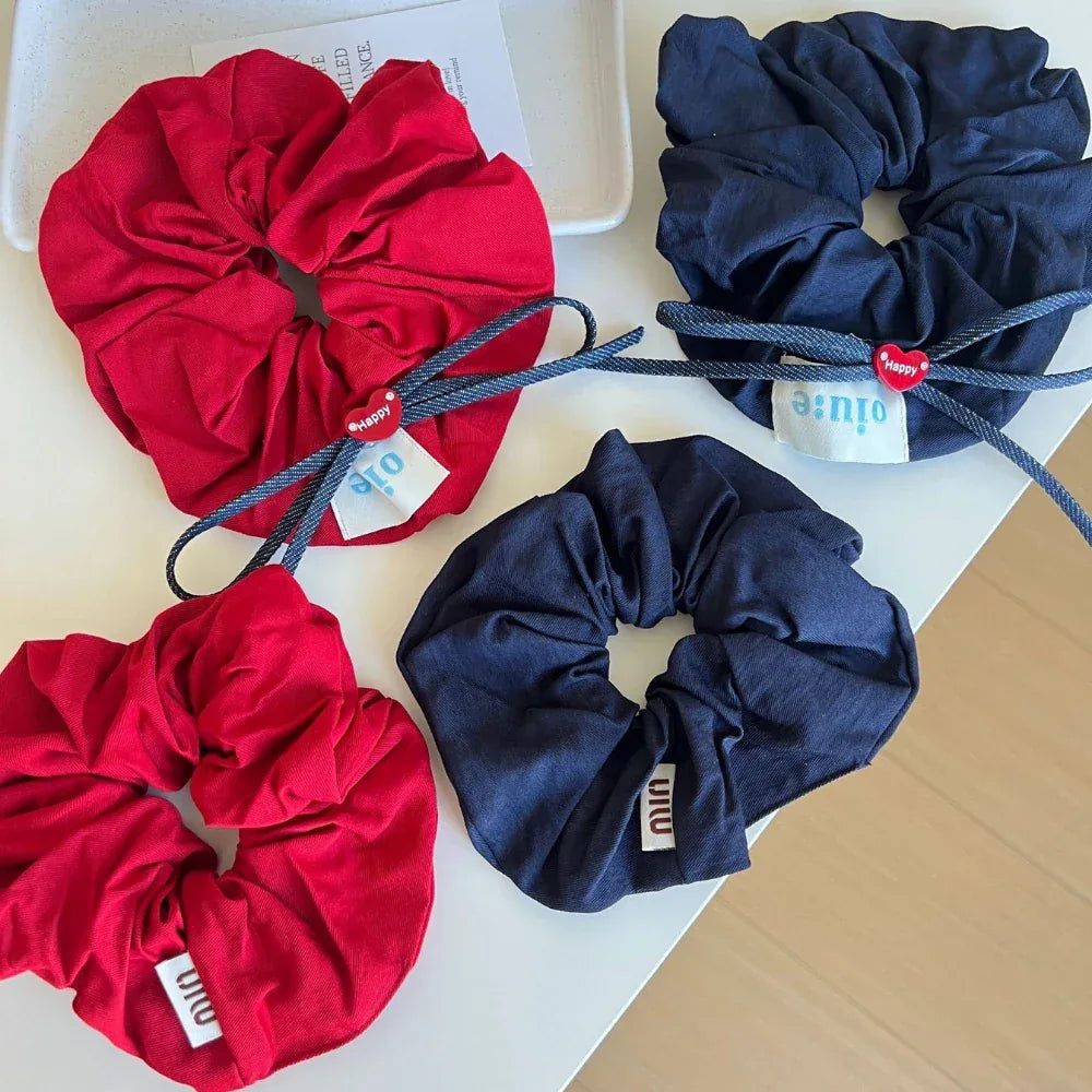 Close-up of red and navy scrunchies featuring bows, heart charms, and fabric tags