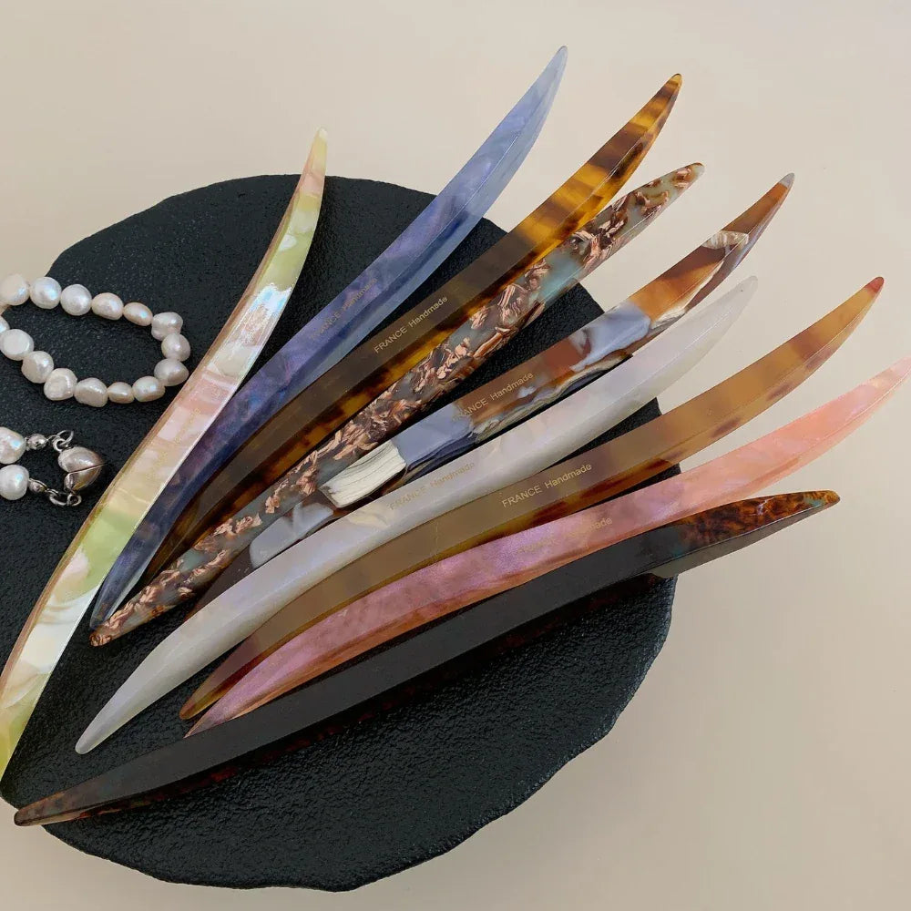 collection of curved marbled acetate hair pins in various colors arranged on a black surface