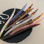 collection of curved marbled acetate hair pins in various colors arranged on a black surface