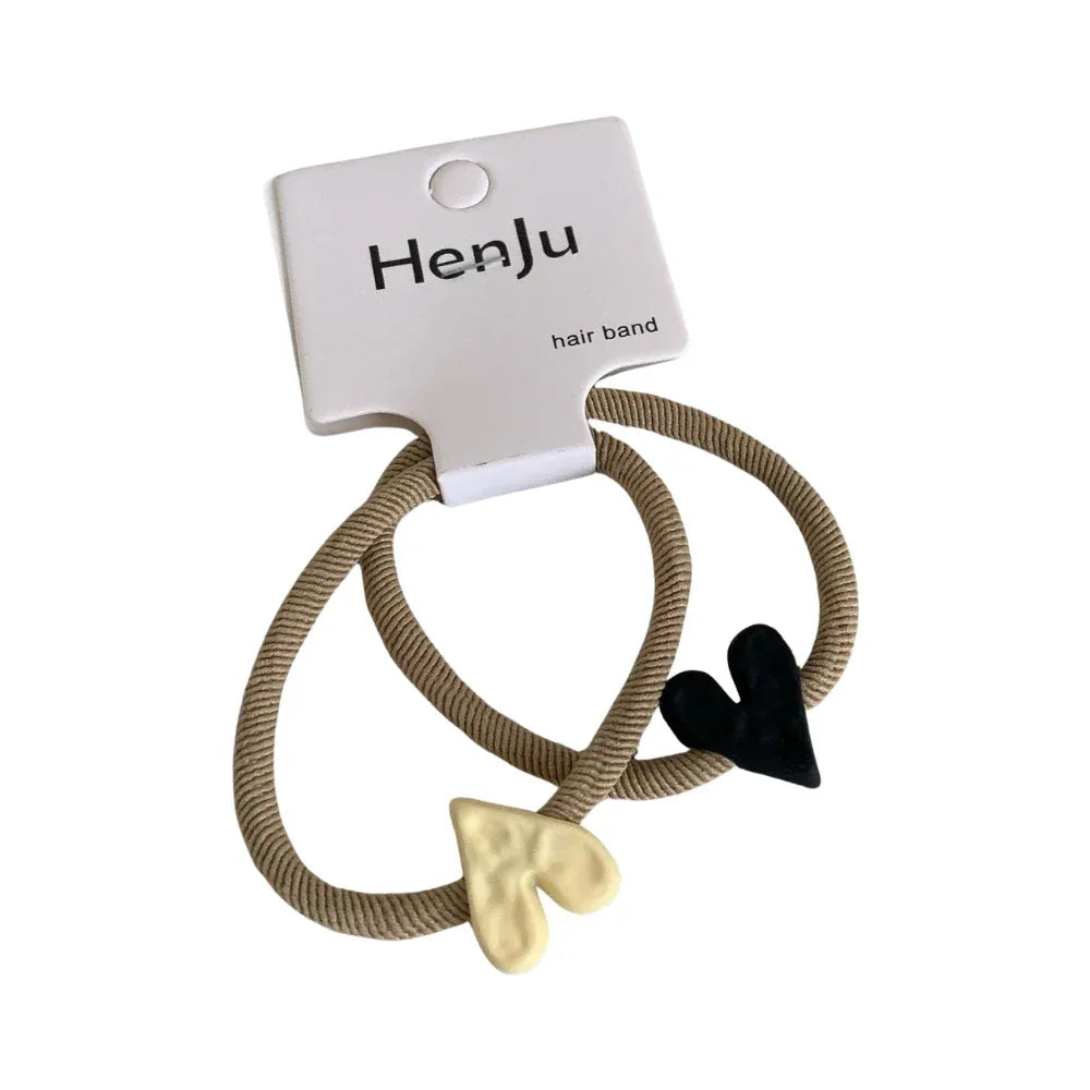 A pair of beige hair ties with black and cream heart charms attached. Main image