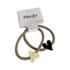 A pair of beige hair ties with black and cream heart charms attached.