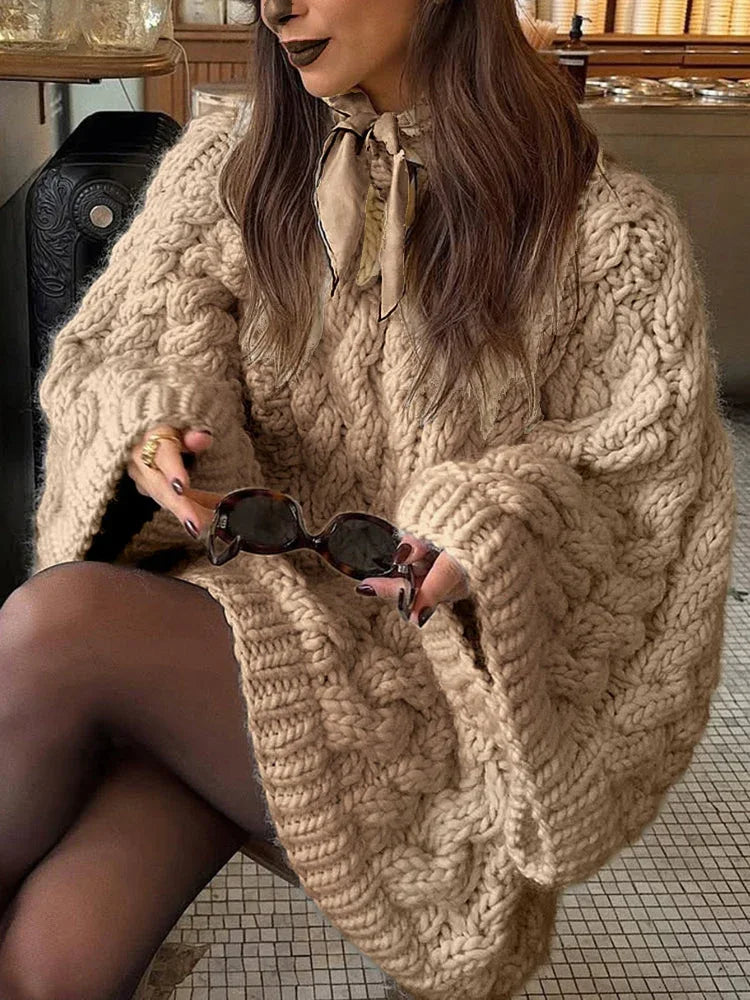 woman wearing a beige chunky cable knit oversized sweater with black tights and holding sunglasses Secondary image