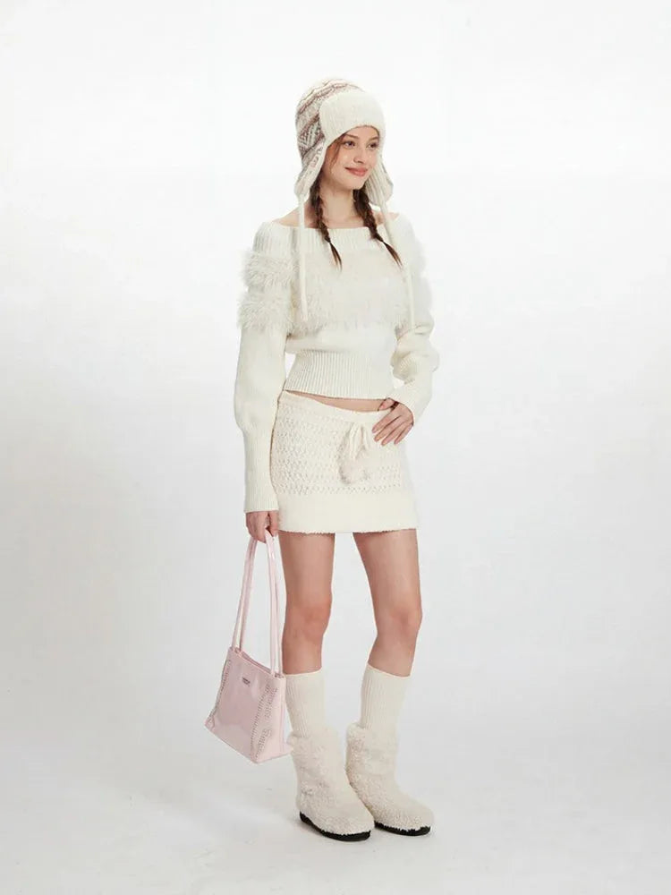Model wearing a white off-the-shoulder sweater and matching mini skirt with a white knit hat, white knee-high socks, and white fuzzy boots. She is holding a pink handbag and posing sideways.