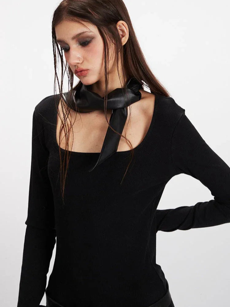Close-up of a woman's face and upper body, wearing a black long-sleeve top with a scarf detail.