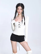 Model posing in a white ribbed long-sleeve top with lace trim and lace-up detail, and black shorts.