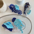 Close-up of a blue seashell hair clip with glitter details