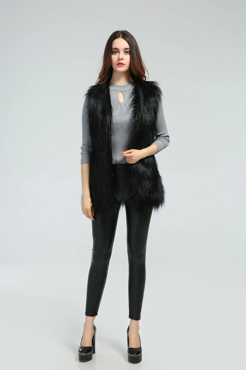 Woman wearing a black faux fur vest over a grey long-sleeved shirt and black leggings