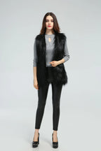 Woman wearing a black faux fur vest over a grey long-sleeved shirt and black leggings