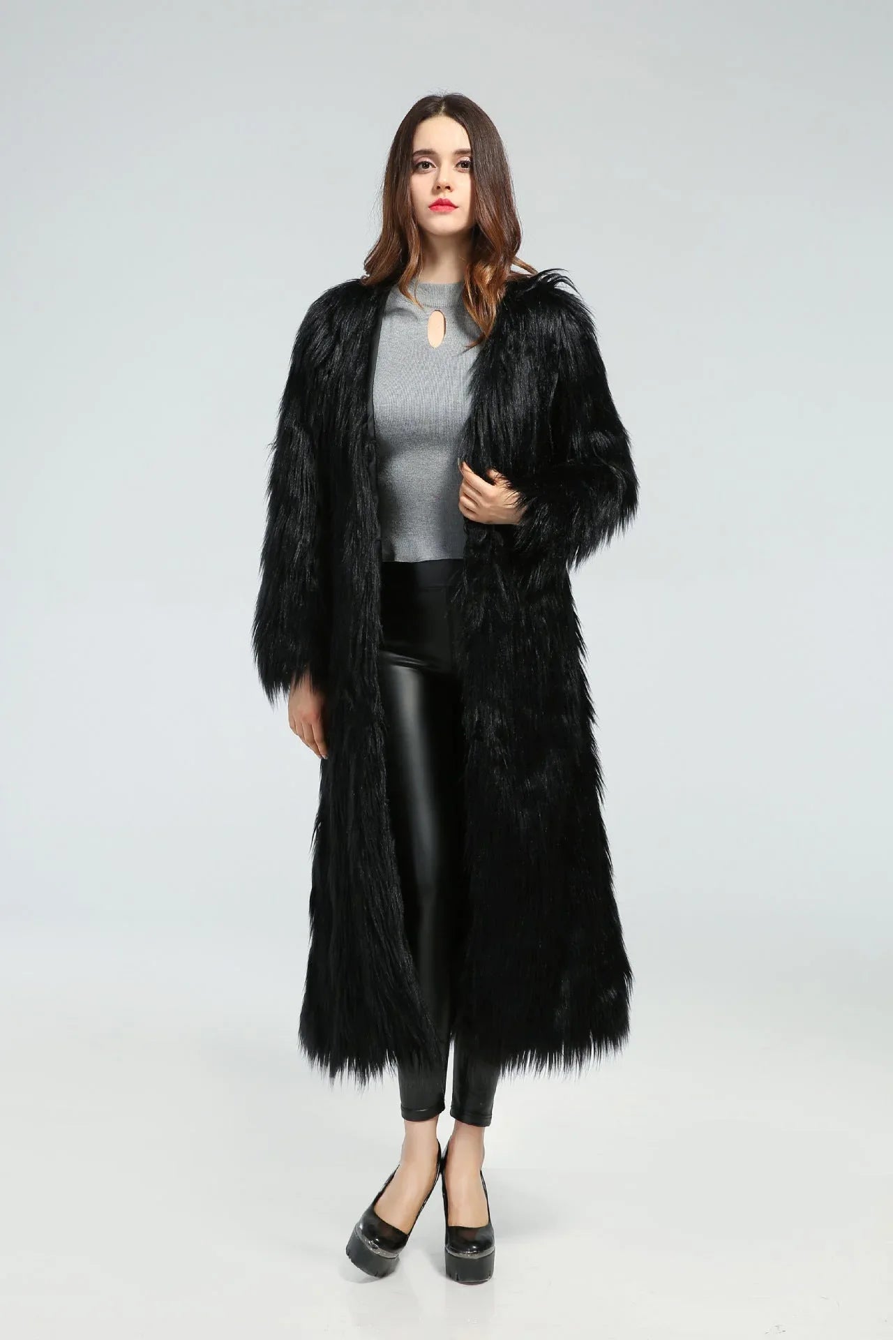 Woman wearing a long black faux fur coat over a grey top and black leggings Main image
