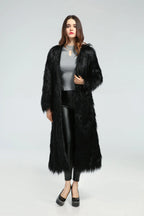 Woman wearing a long black faux fur coat over a grey top and black leggings
