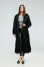 Woman wearing a long black faux fur coat over a grey top and black leggings