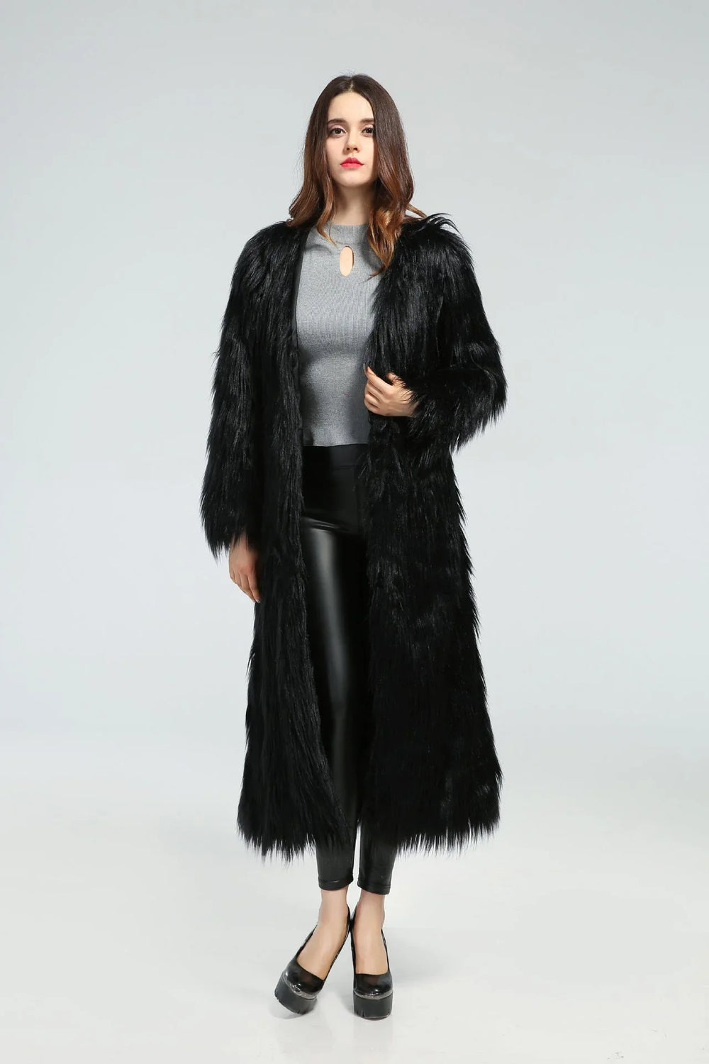 Woman wearing a long black faux fur coat over a grey top and black leggings