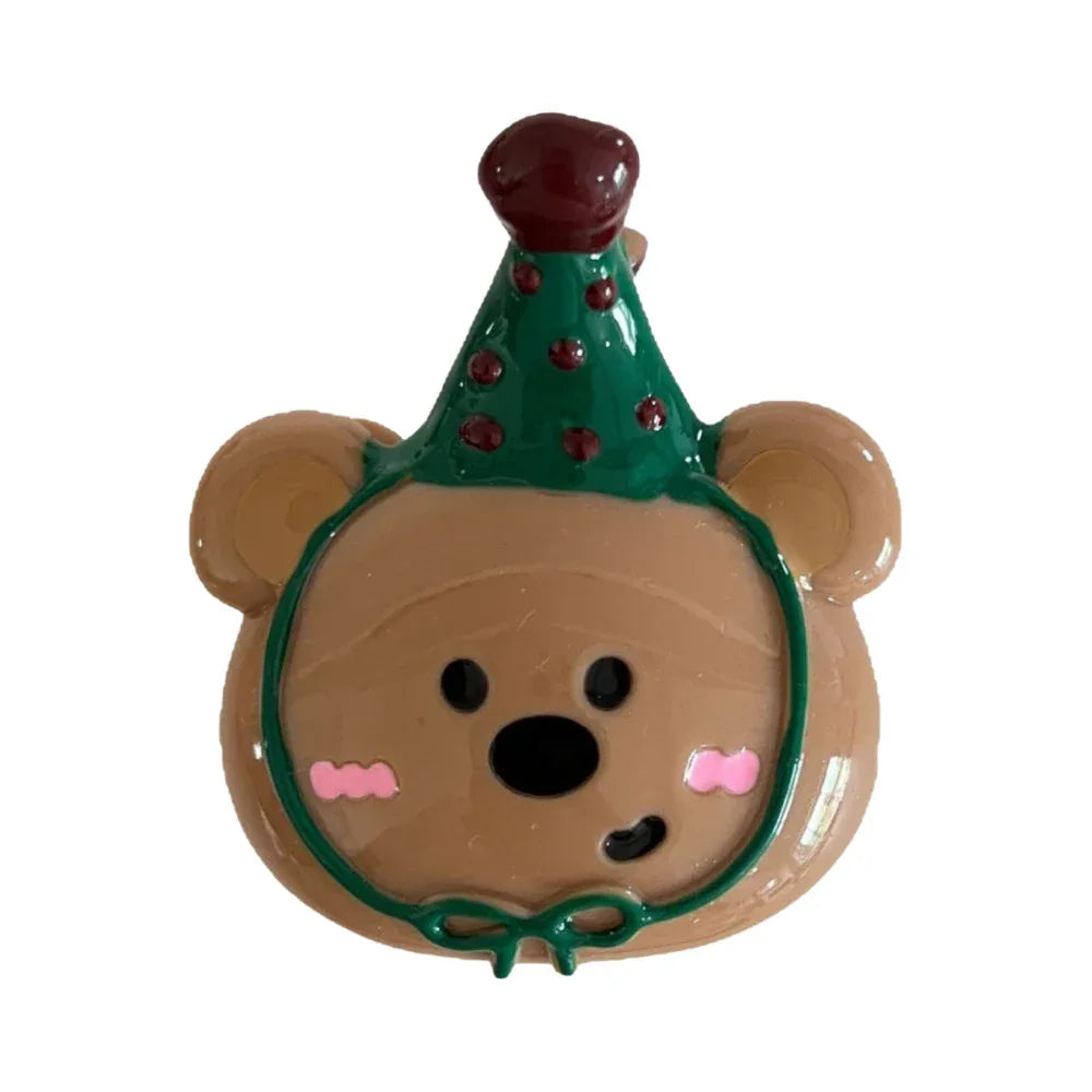 Close-up of a brown bear-shaped hair clip with a green party hat and red polka dots. Main image