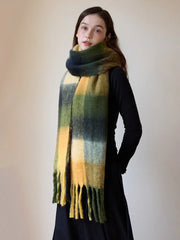 Woman standing with a long, oversized plaid scarf with fringe detail draped around her neck and shoulders.