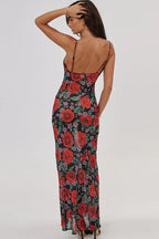 Woman wearing a long floral print dress with spaghetti straps and a cowl neckline, back view.