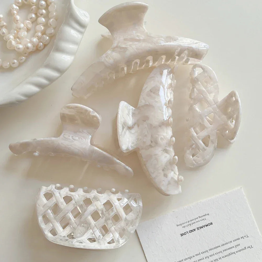 Assortment of cream-colored marbled acetate hair clips and a pearl necklace on a white tabletop.