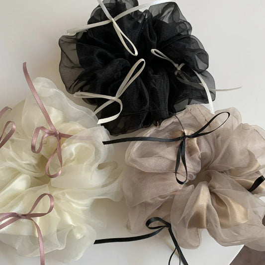 A collection of three large scrunchies in ivory, black, and taupe, each with contrasting ribbon accents.