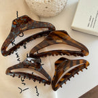 Four tortoiseshell claw hair clips of varying sizes arranged on a white surface with decorative items.
