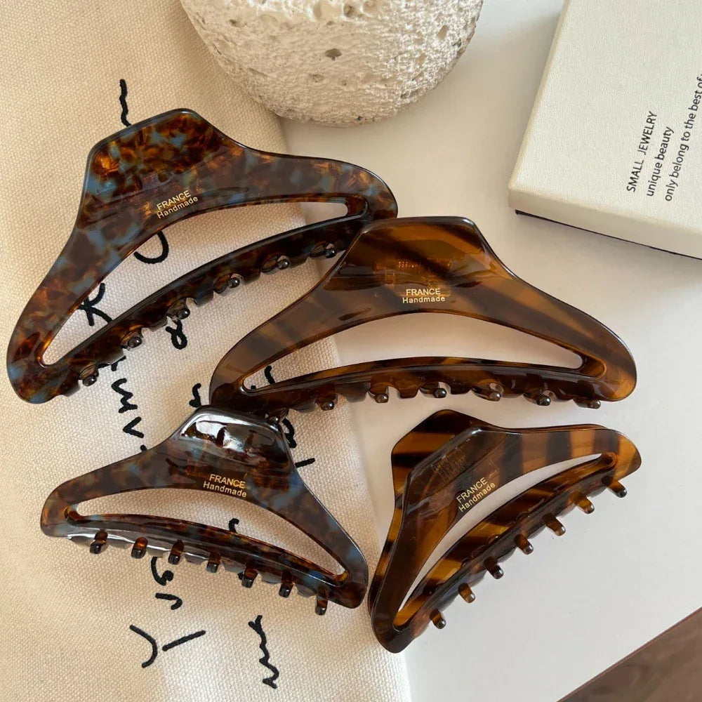 Four tortoiseshell claw hair clips of varying sizes arranged on a white surface with decorative items.