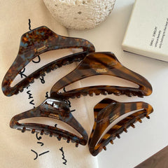 Four tortoiseshell claw hair clips of varying sizes arranged on a white surface with decorative items.