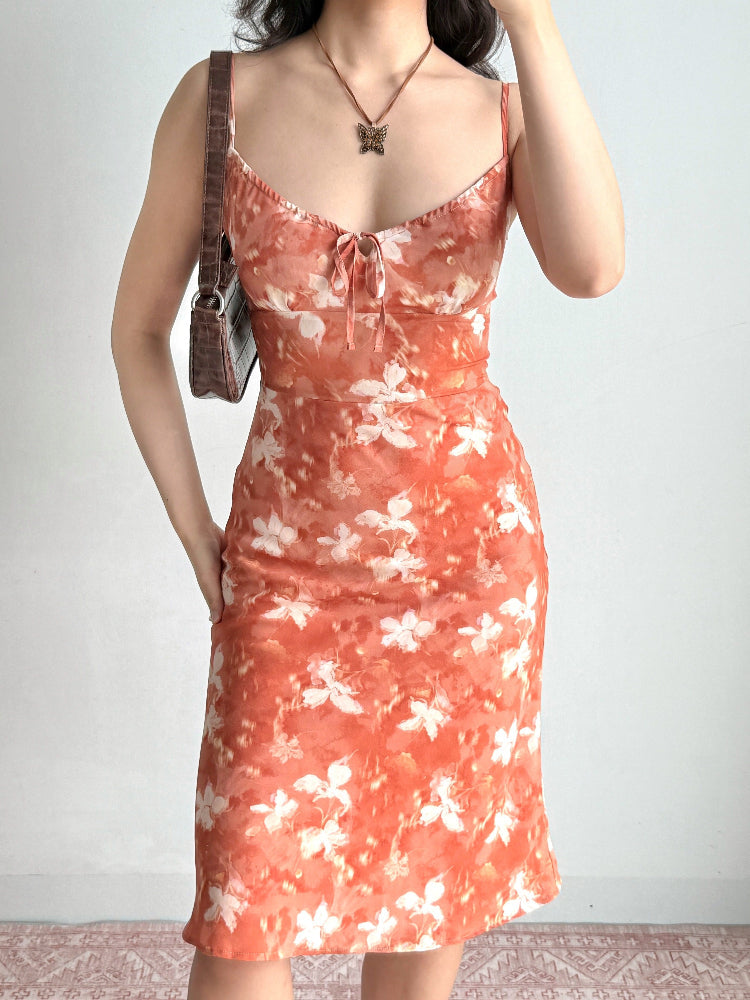 Woman holding a brown crocodile-embossed handbag while wearing a floral print midi slip dress.