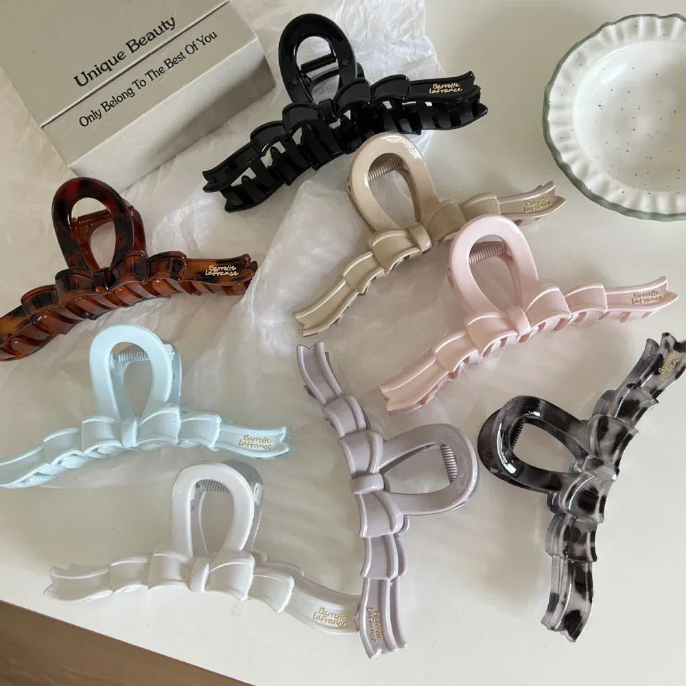 A collection of bow claw clips in various colors including black, beige, pink, grey, blue, white, and tortoiseshell.