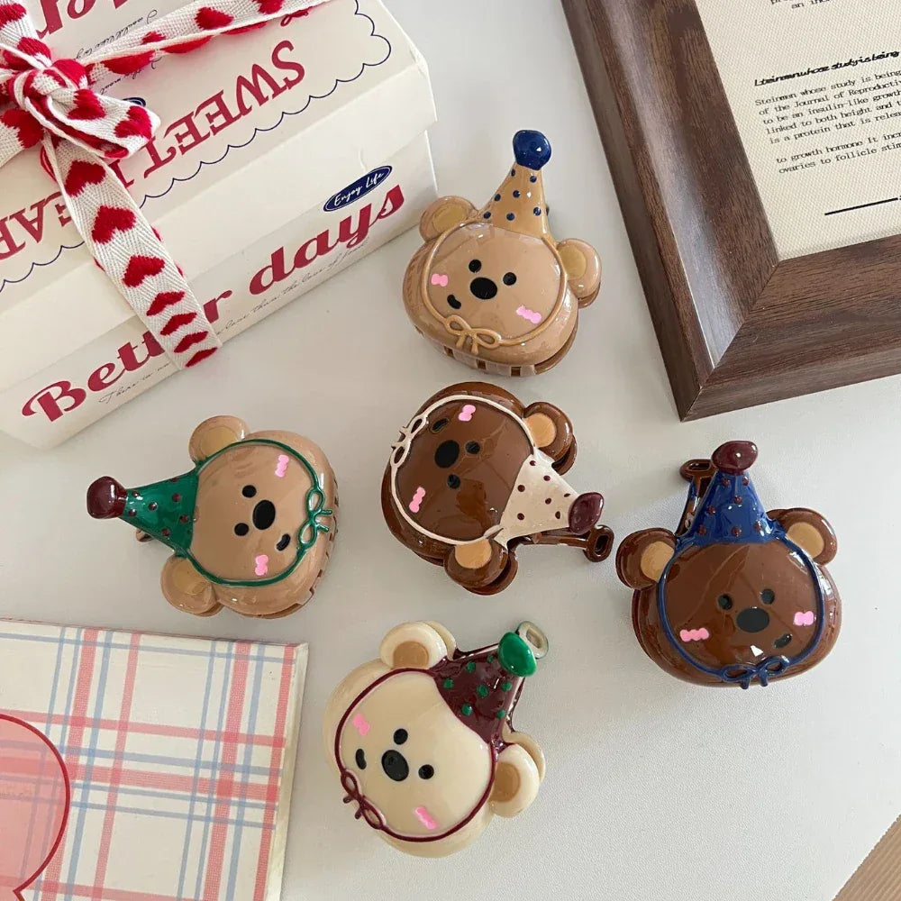 Overhead view of five bear-shaped hair clips with party hats, showcasing different color combinations and designs, placed on a table.