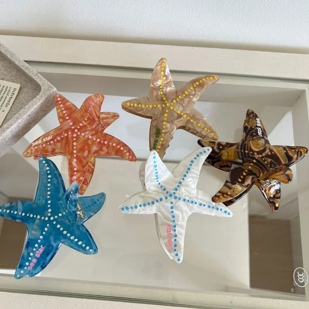 Collection of five starfish hair clips in various colors (orange, yellow, brown, blue, white) arranged on a glass surface
