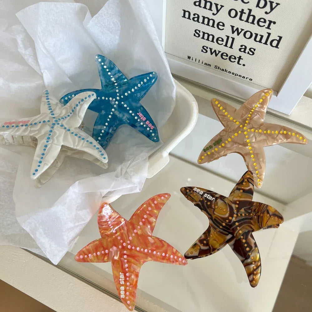 Four starfish hair clips (white, blue, yellow, orange) displayed in a white basket with crumpled paper