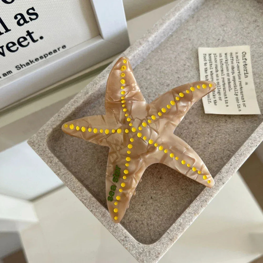 Tan marbled starfish hair clip with yellow dots and "sea star" text, resting in a gray tray